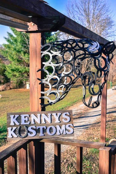 Kenny’s Kustoms sign with a black-and-white metal cow head mounted on a wooden fence outdoors