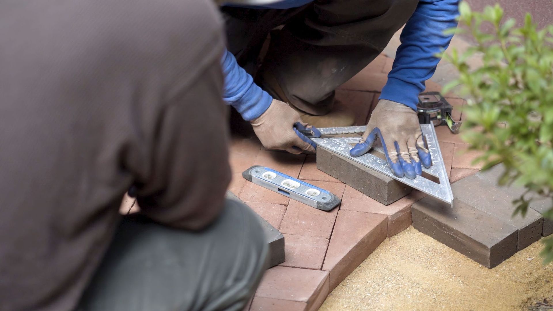 Workers laying red paving stones with hand tools on a walkway