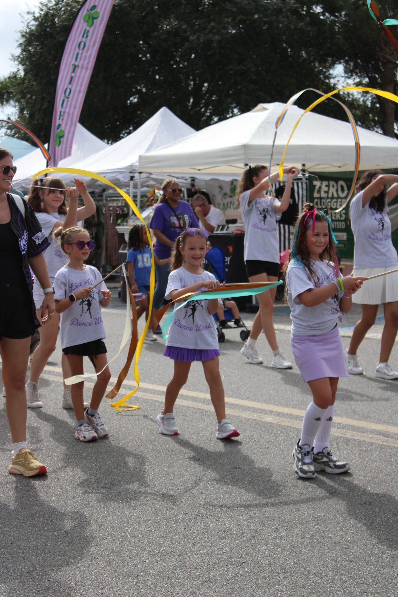 Children with hula hoops marching in a street parade past white tents and banners