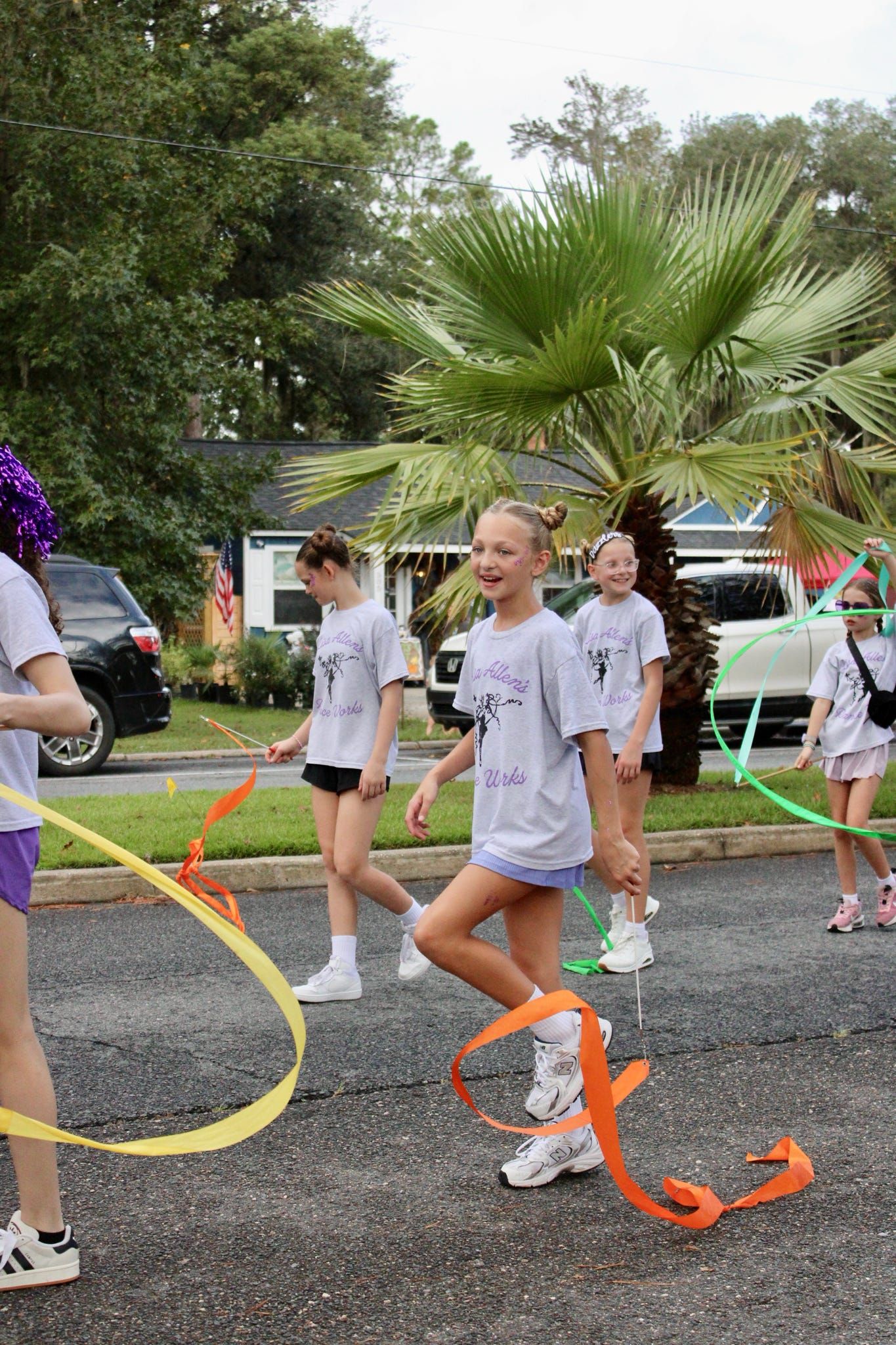 Children in white shirts walk in a park parade with colorful ribbons and streamers