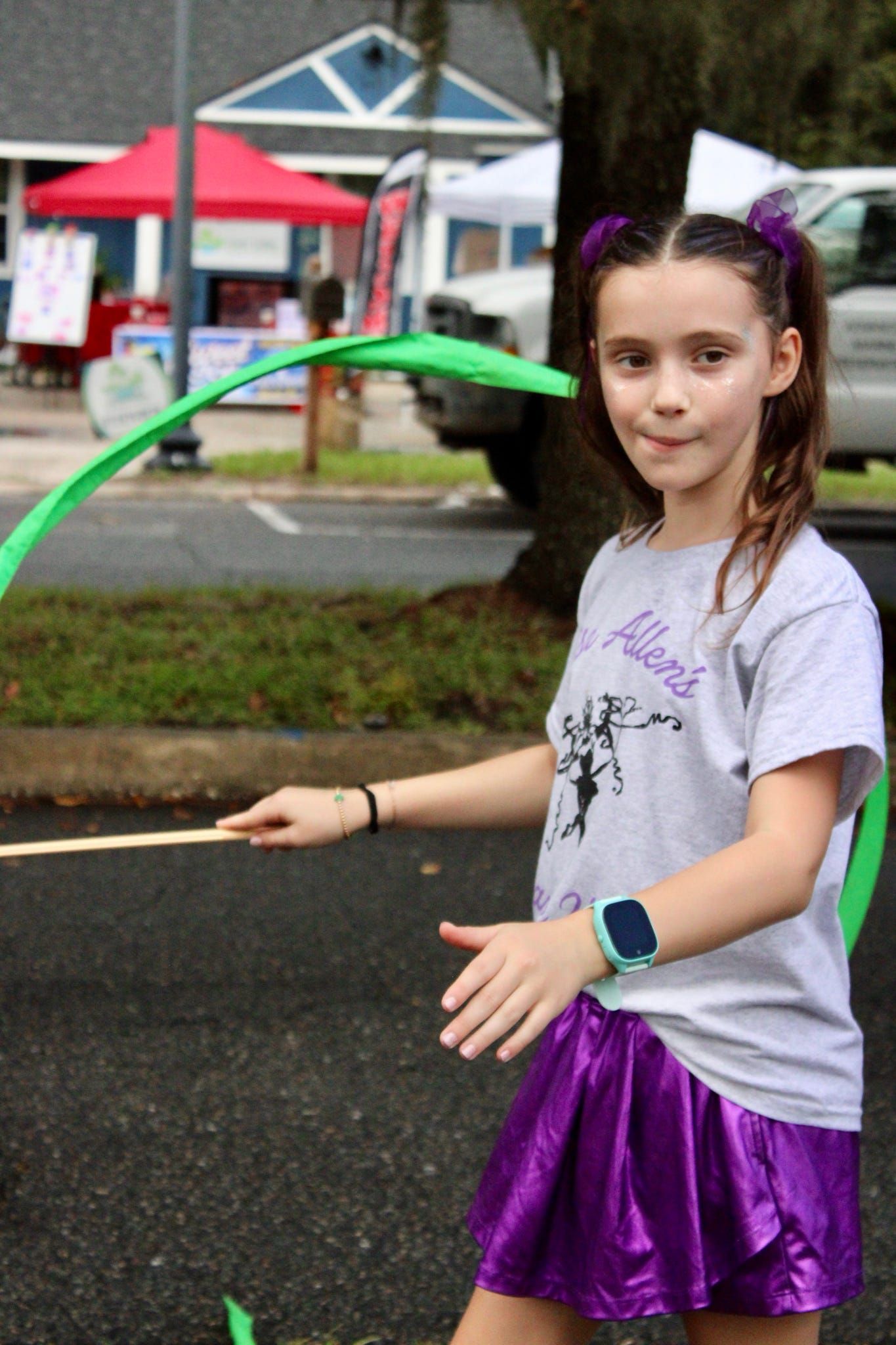 Girl with purple hula hoop standing outdoors on a wet street in front of a house.