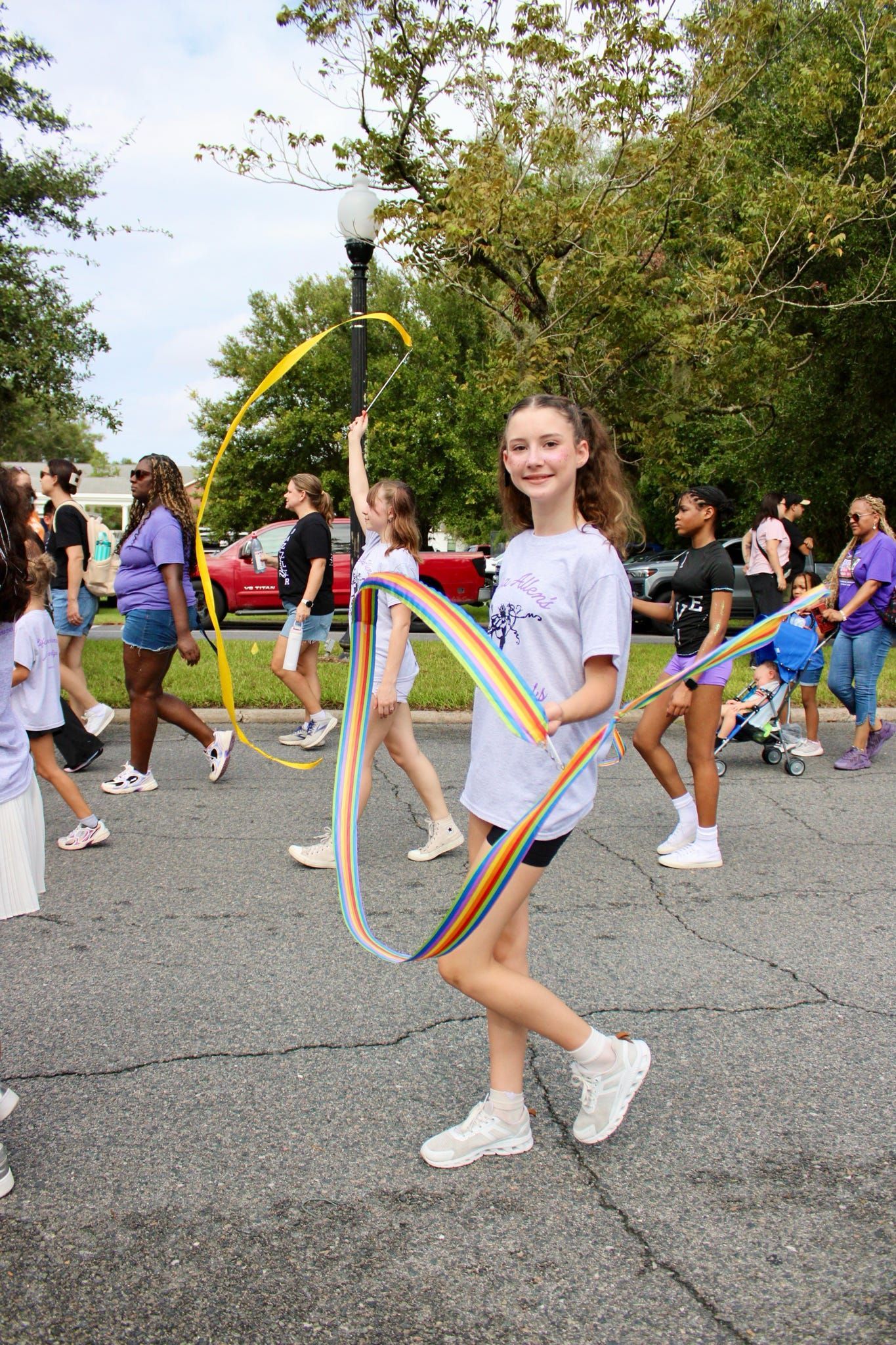 Girl twirling colorful ribbon in a parade on a tree-lined street