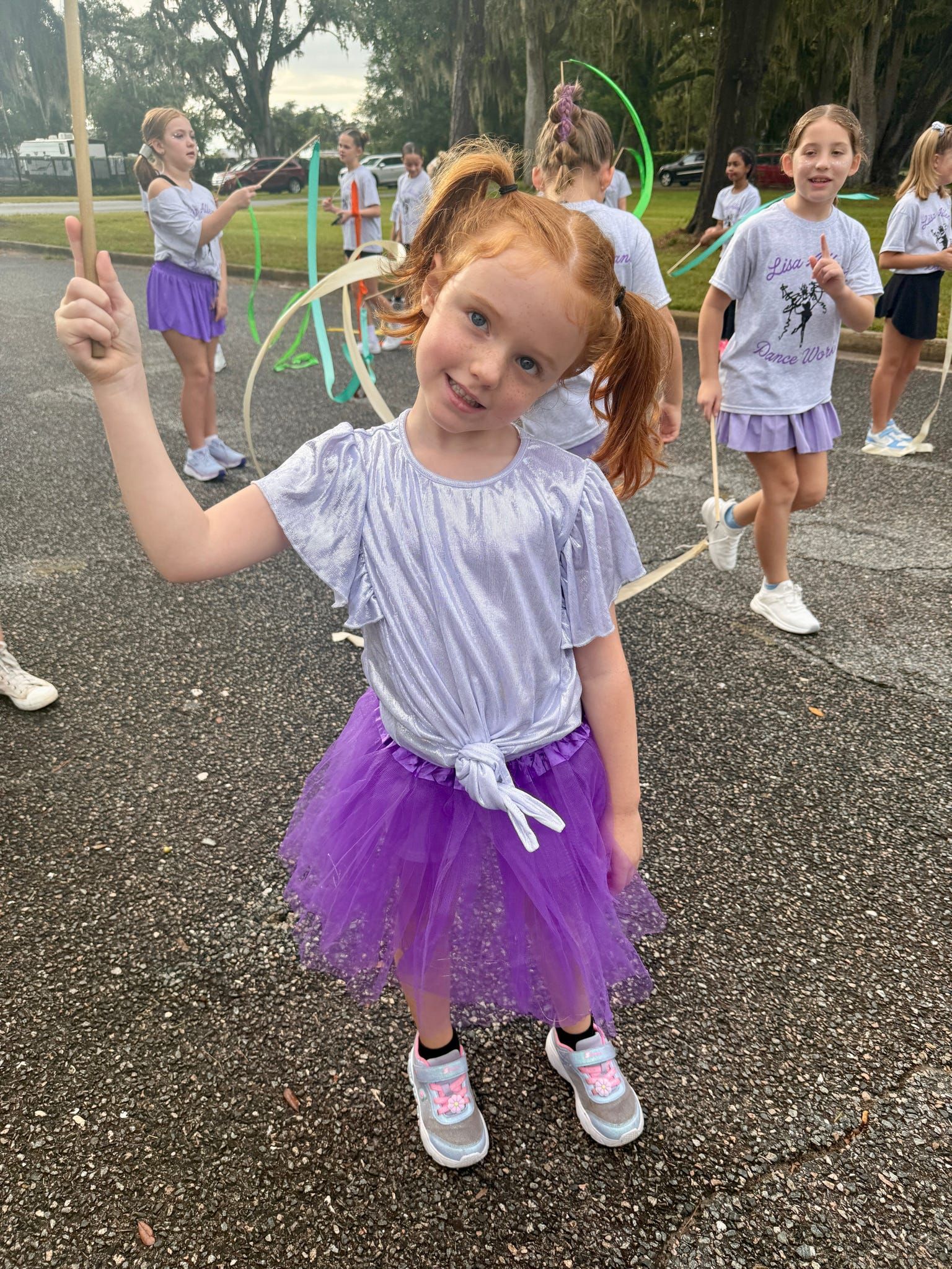 Child in a purple tutu smiles and points at a sidewalk bubble play area outdoors.