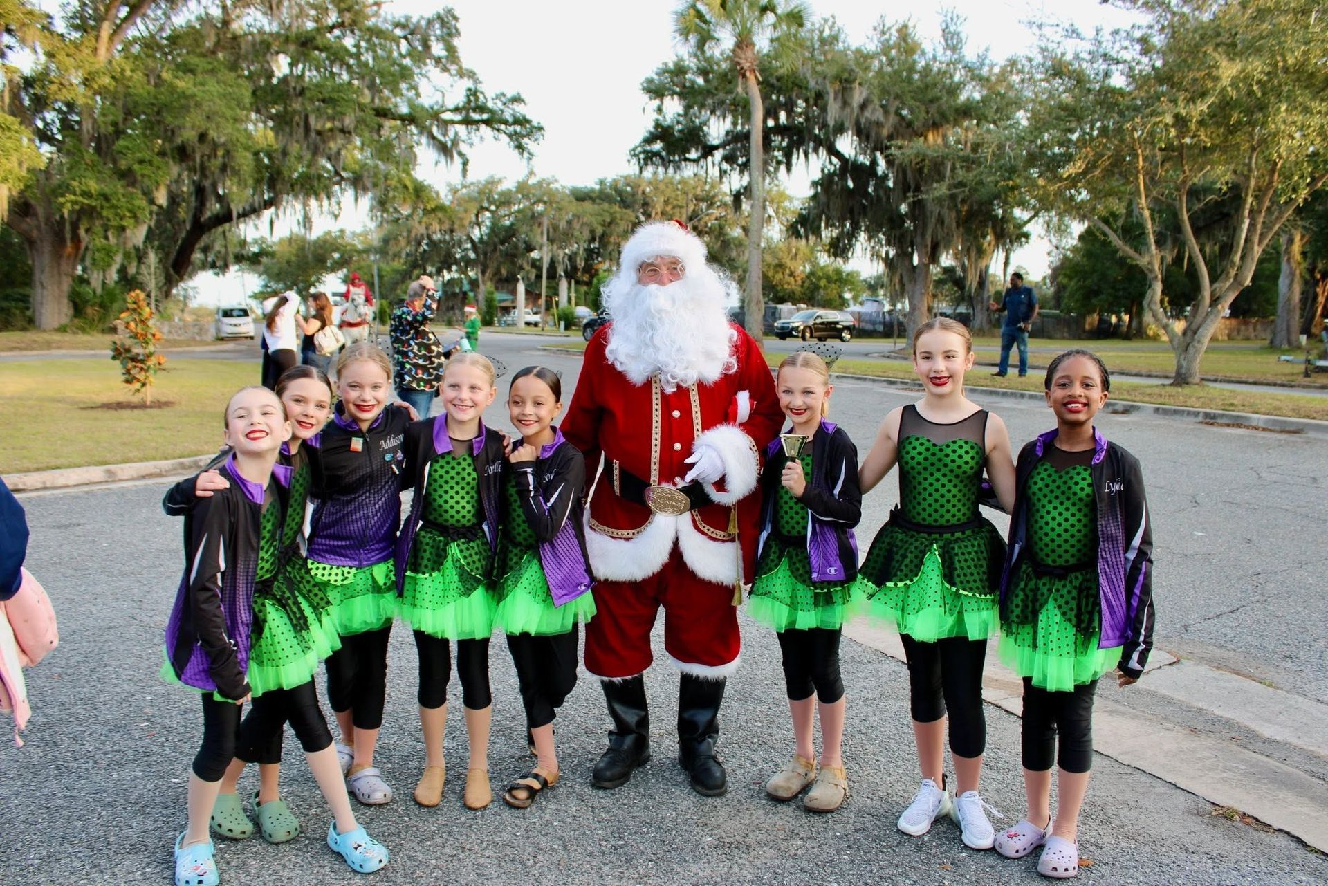 Group in green and black outfits posing with Santa outdoors in a park