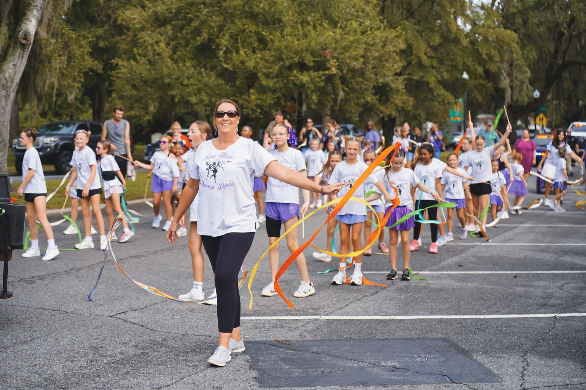 Group of people in white shirts doing a ribbon dance outdoors on a paved road.