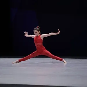 Dancer in a red costume holds a wide split pose on a stage with a dark background