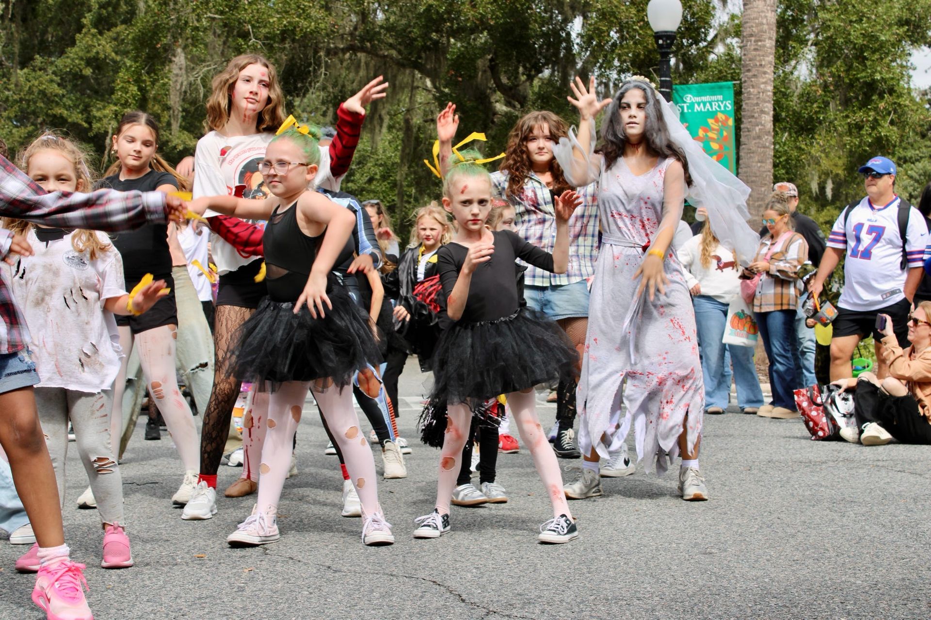 Children in costumes marching in a street parade, with dancers and spectators in the background