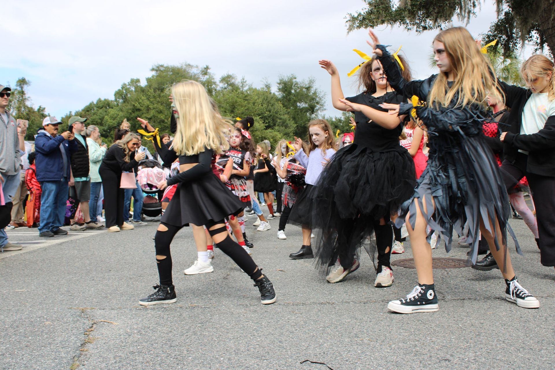 Dancers in black and silver costumes perform outdoors before a crowd at a street festival