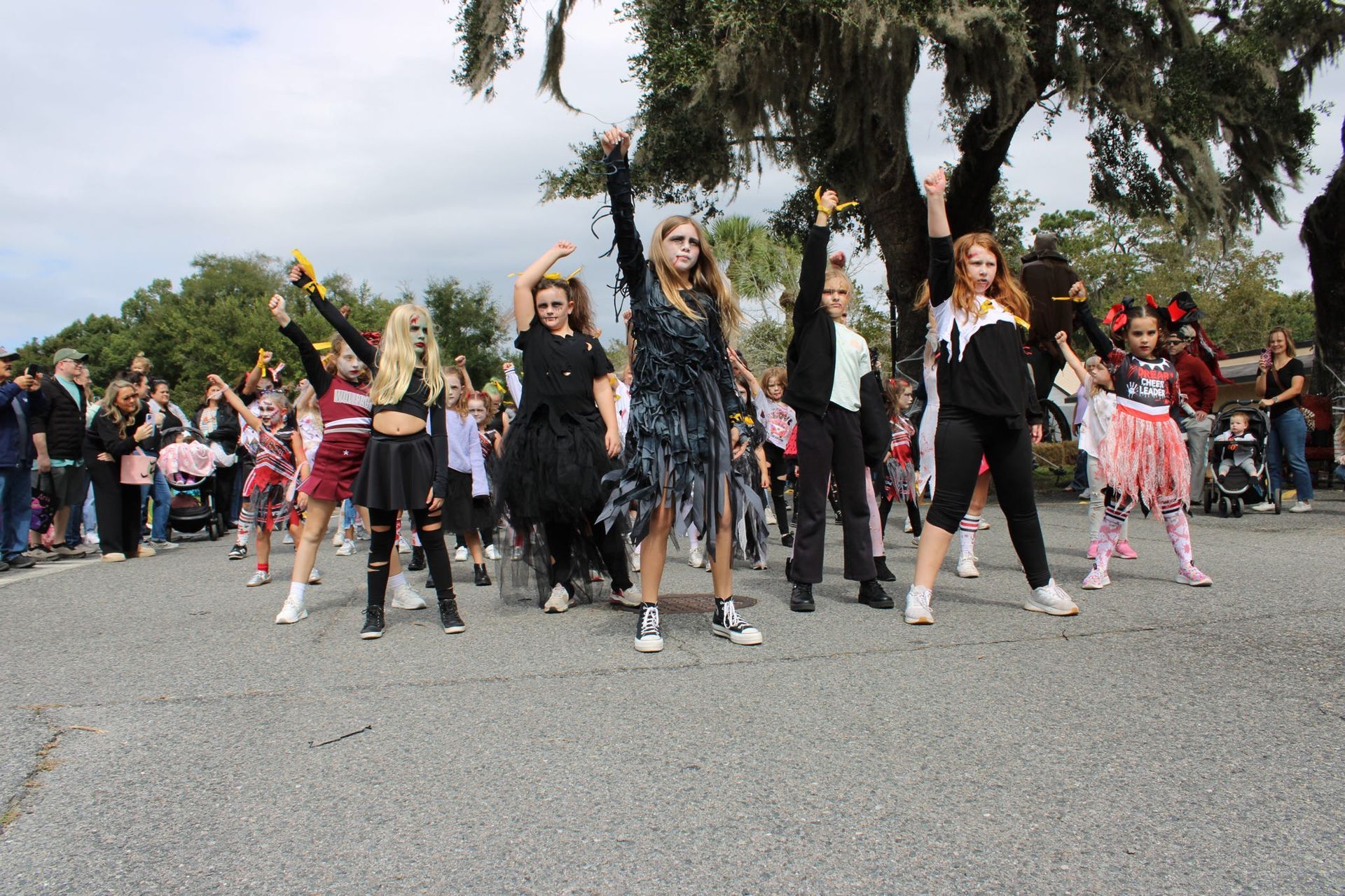 Group of dancers performing outdoors on a street, wearing black costumes with colorful accents, spectators behind them