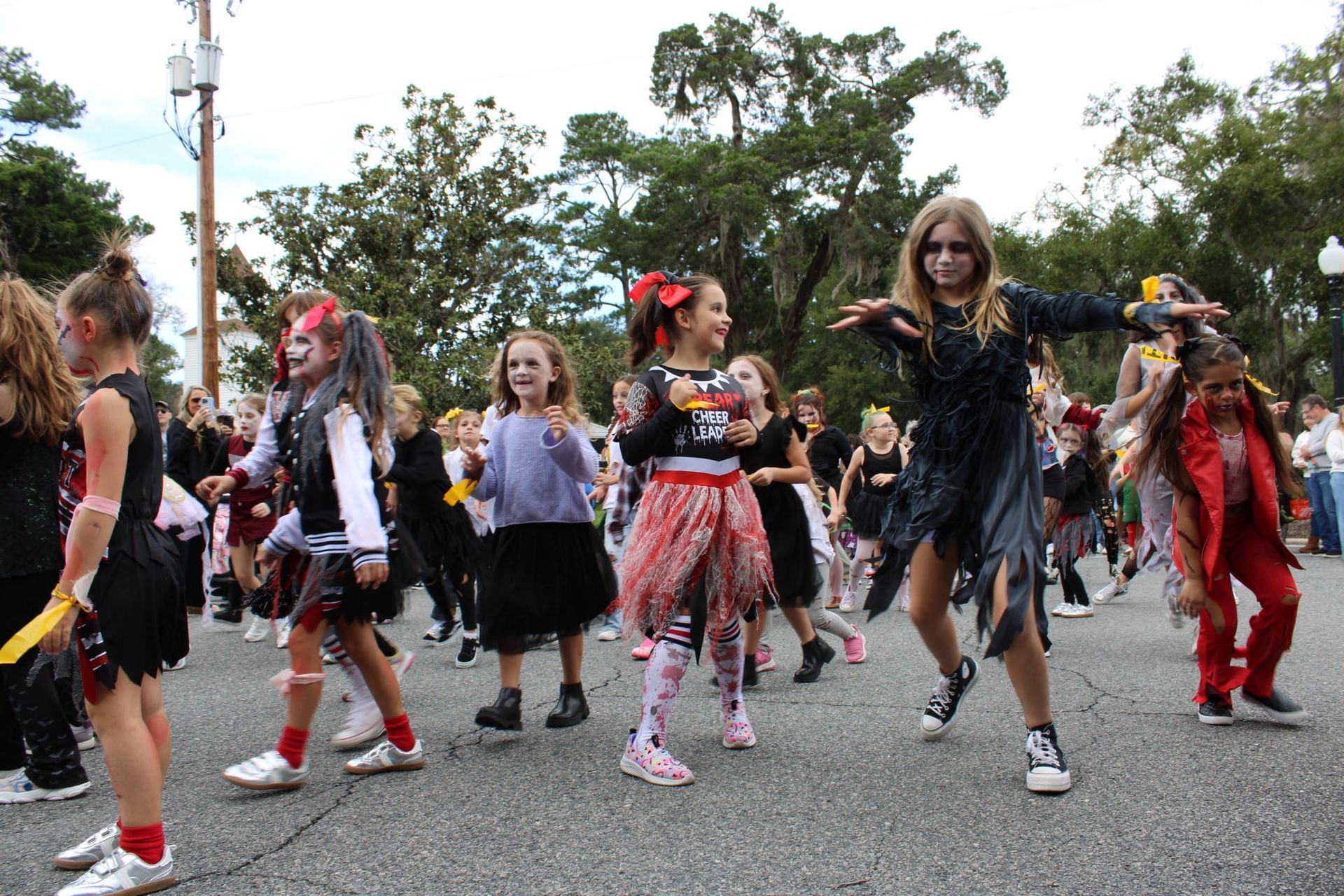 People in Halloween costumes walking in a parade on a tree-lined street