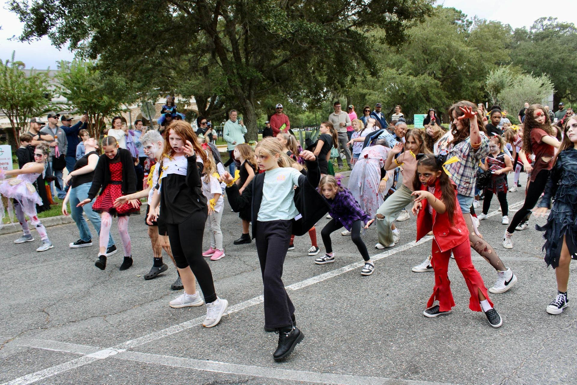 Children dancing together outdoors in a park, with one in red and others in colorful outfits.