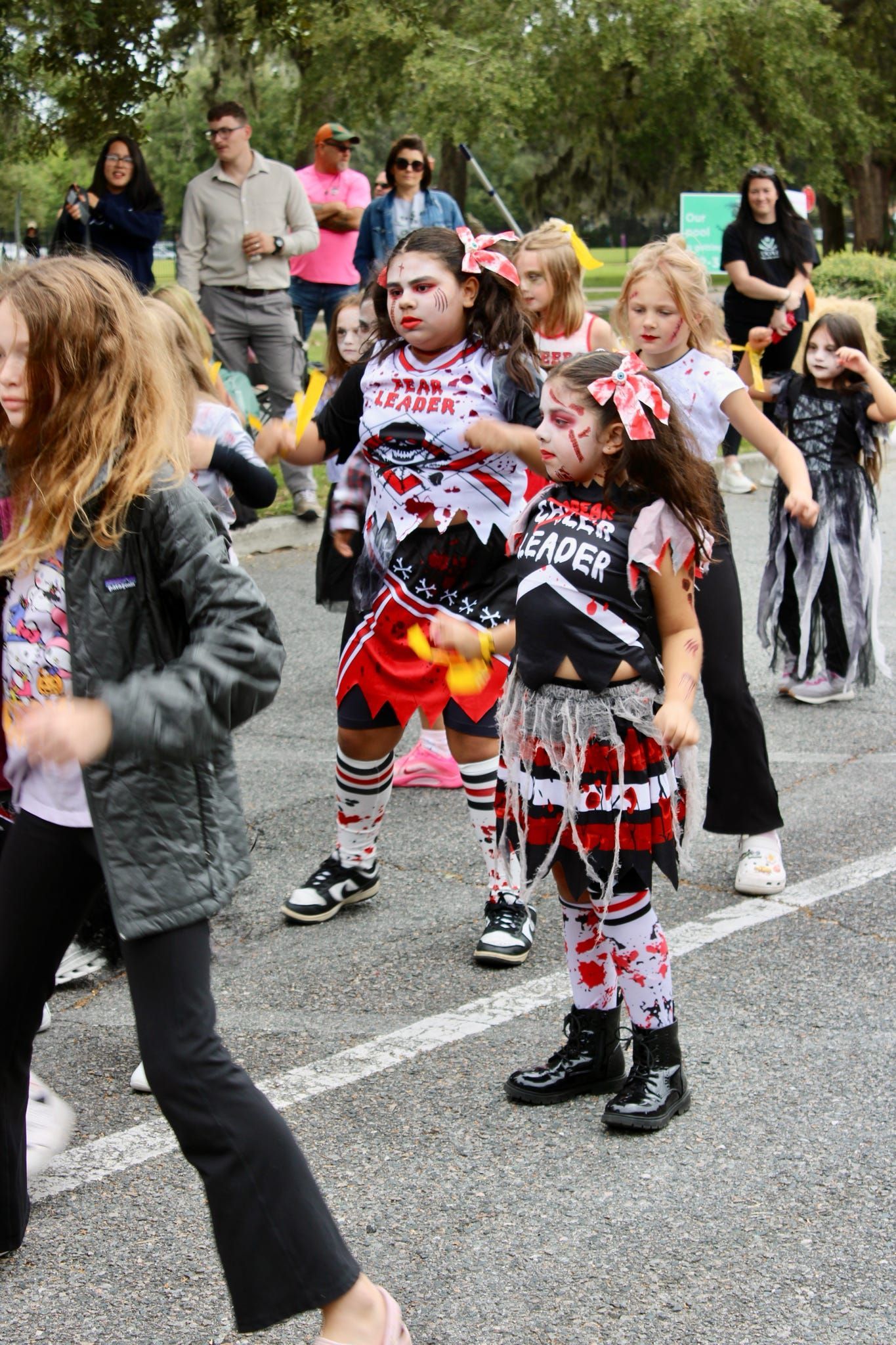 Children in colorful costumes marching in a parade on a road, with spectators watching nearby