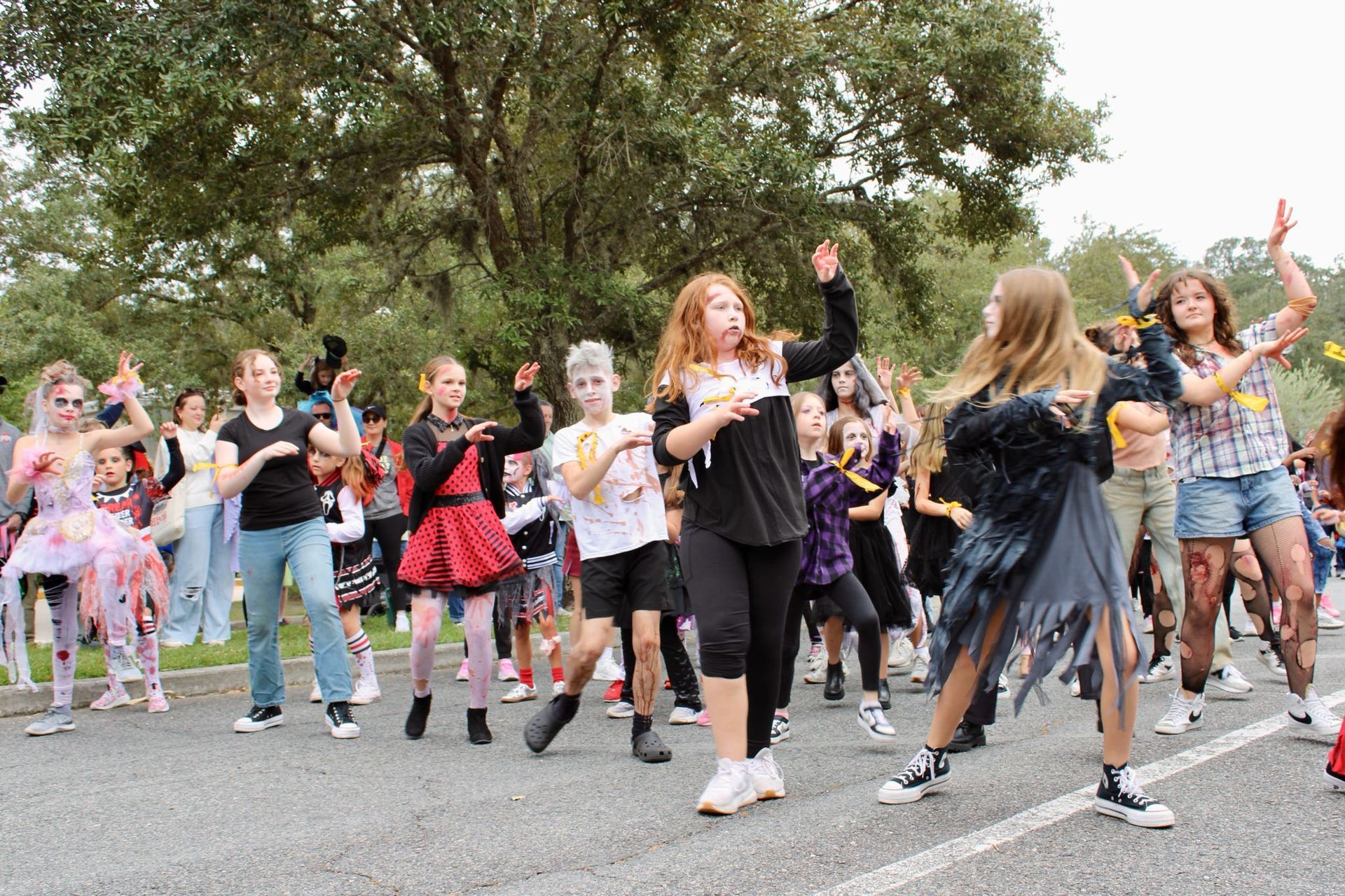 Group of people dancing outdoors in a park, wearing colorful costumes and casual clothes.