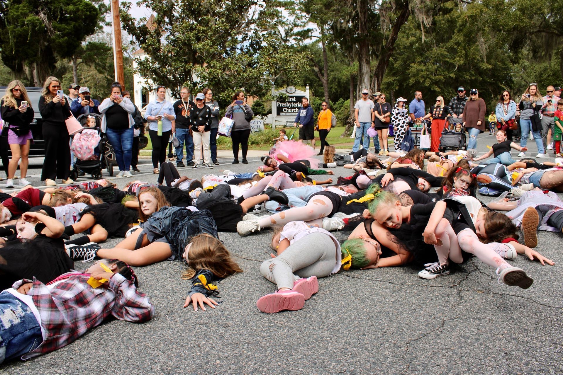 People lying face down on a street while a crowd watches during a public protest