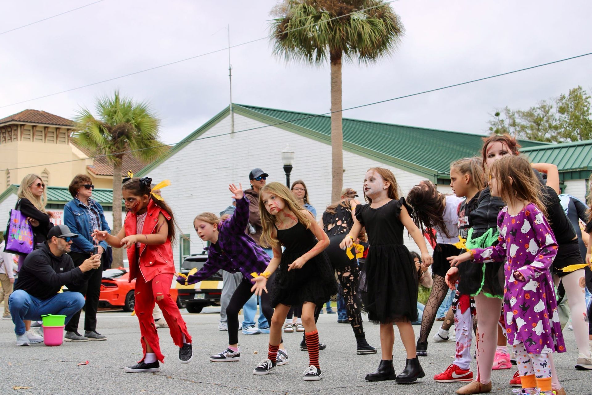 Group dancing outdoors in colorful costumes on a street, with spectators watching nearby