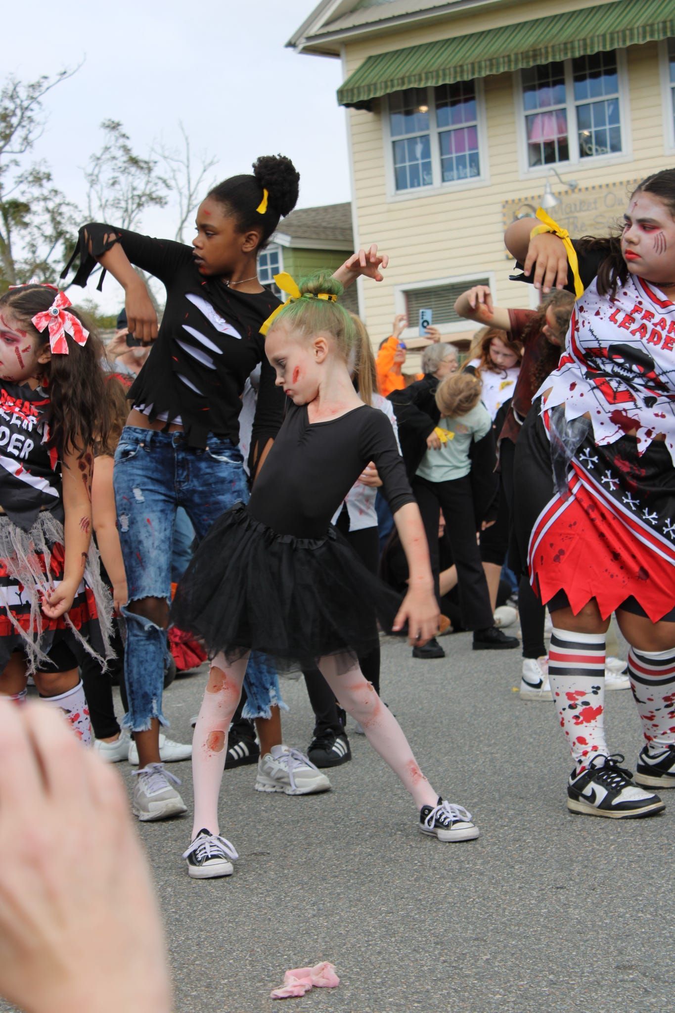 Children in costumes dancing in a street parade, with one girl in a black dress in the foreground