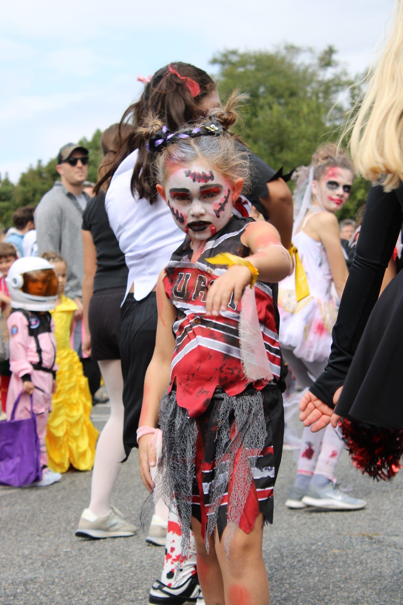Child in a colorful costume and face paint standing outdoors at a parade or festival