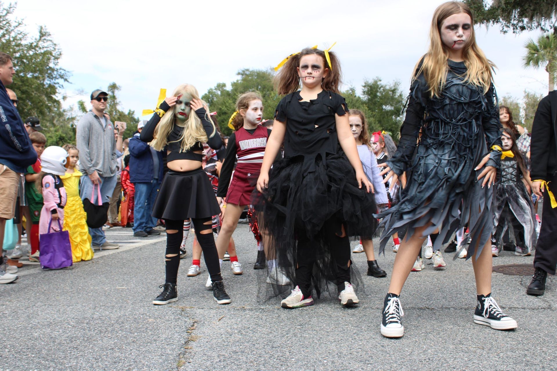People in dark costumes marching in a street parade, with spectators lining the roadside.
