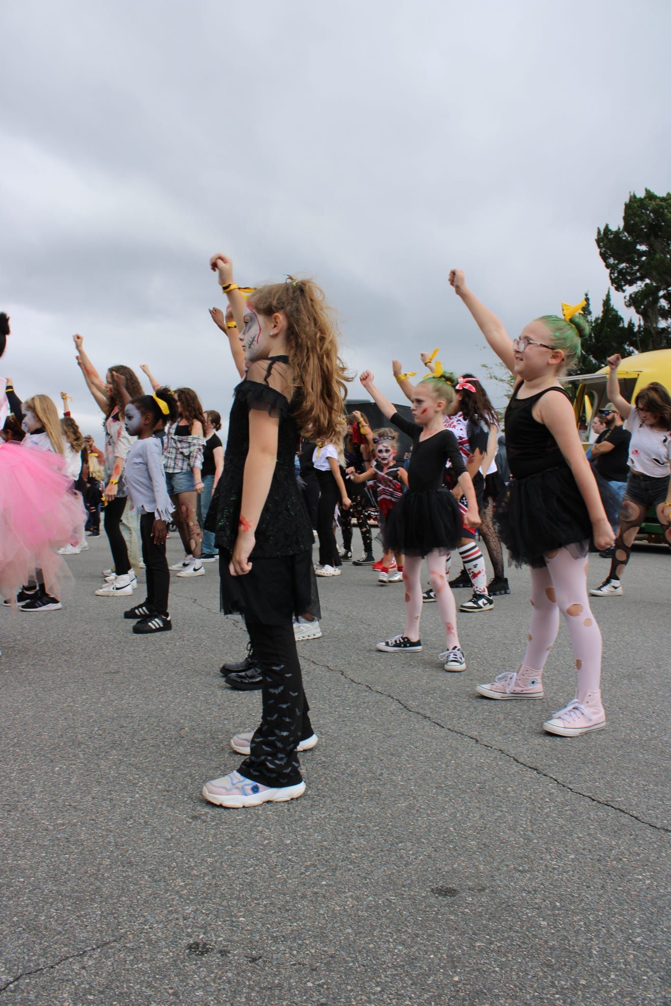 Children in black costumes dance in formation outdoors on a paved street.