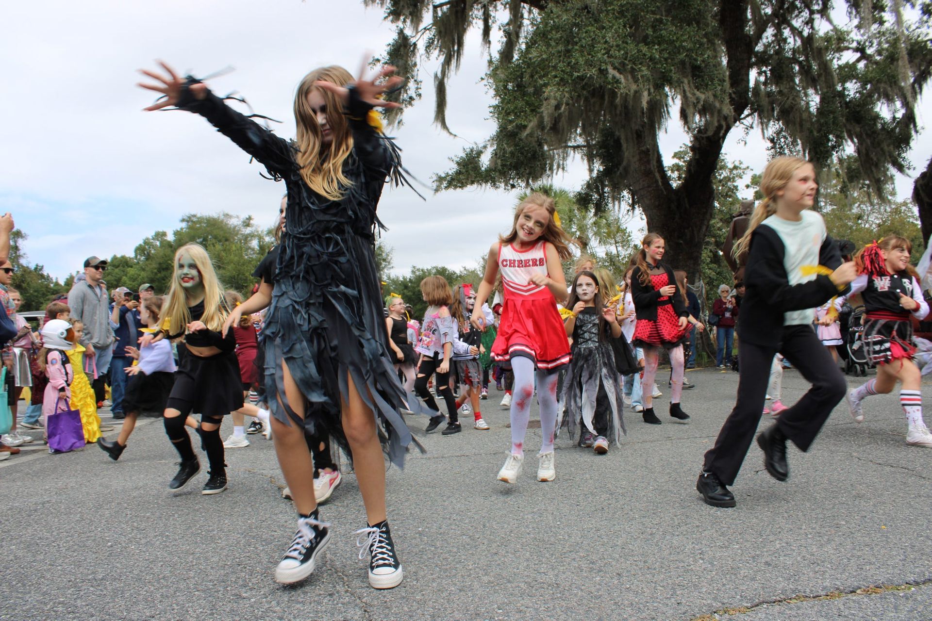 Costumed dancers performing outdoors in a street parade, with arms raised and spectators behind them