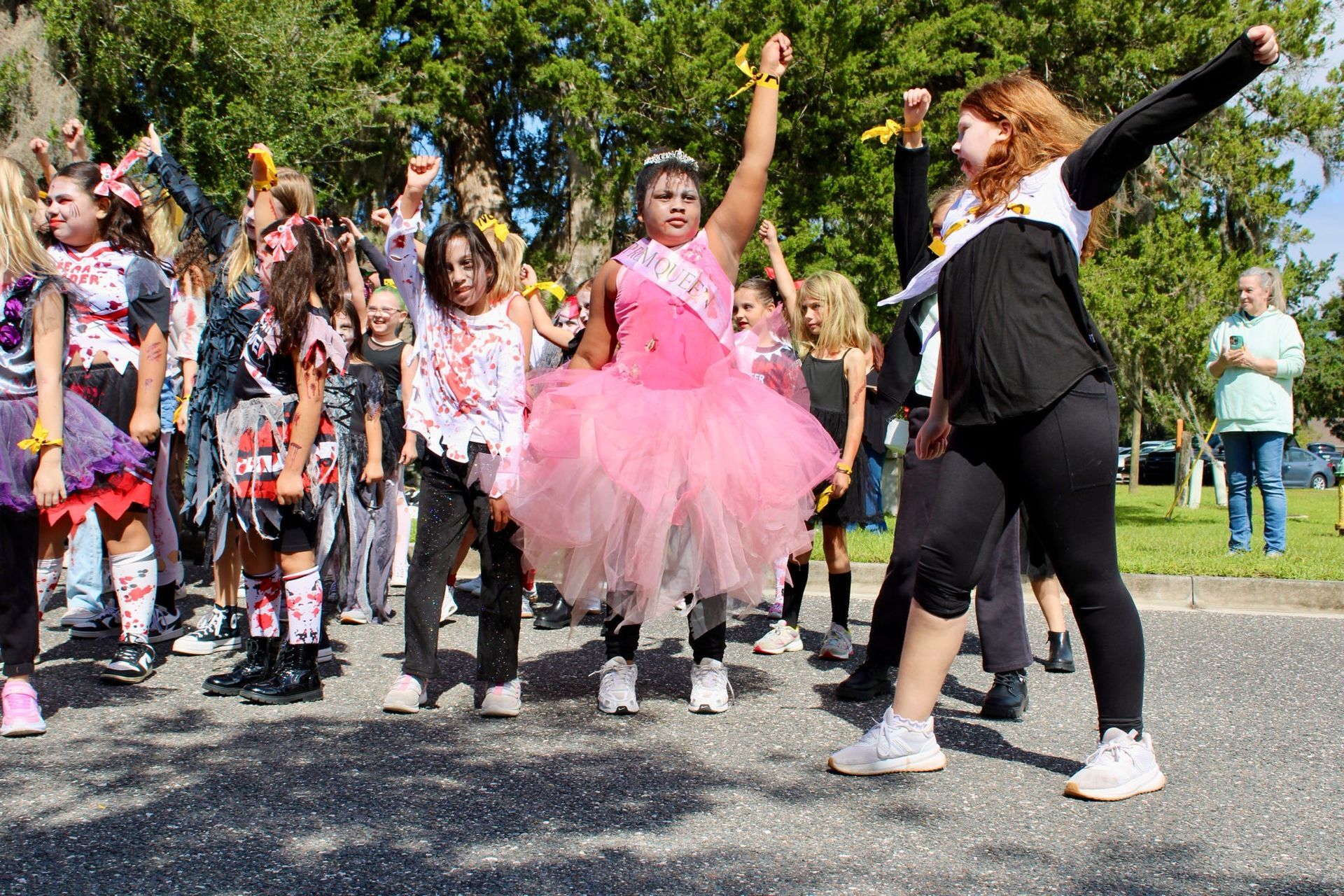 Children dancing outdoors, with a child in a pink tutu and another in black leading the group.