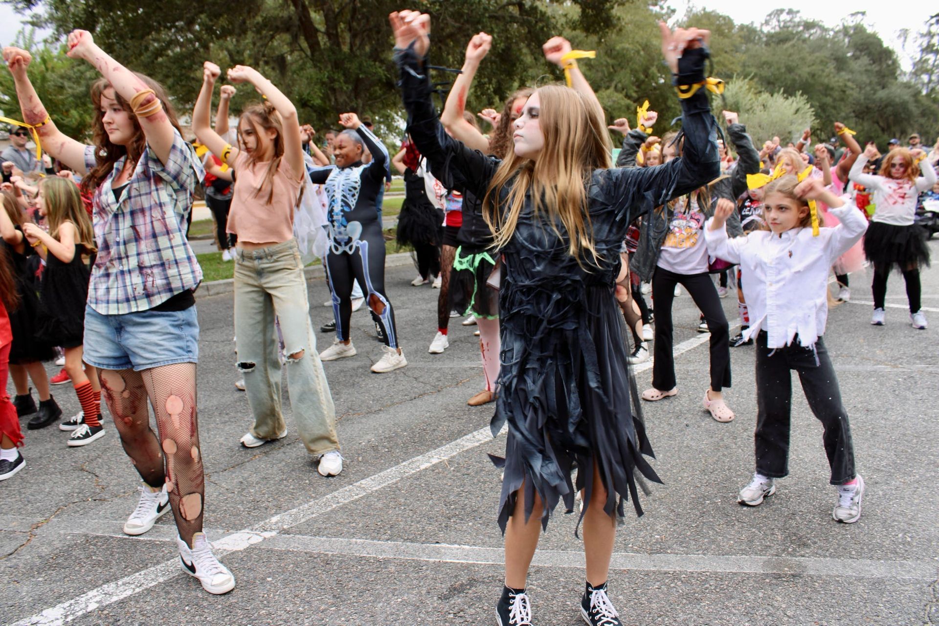 Group of people dancing in a street parade, arms raised, with a crowd and trees in the background.