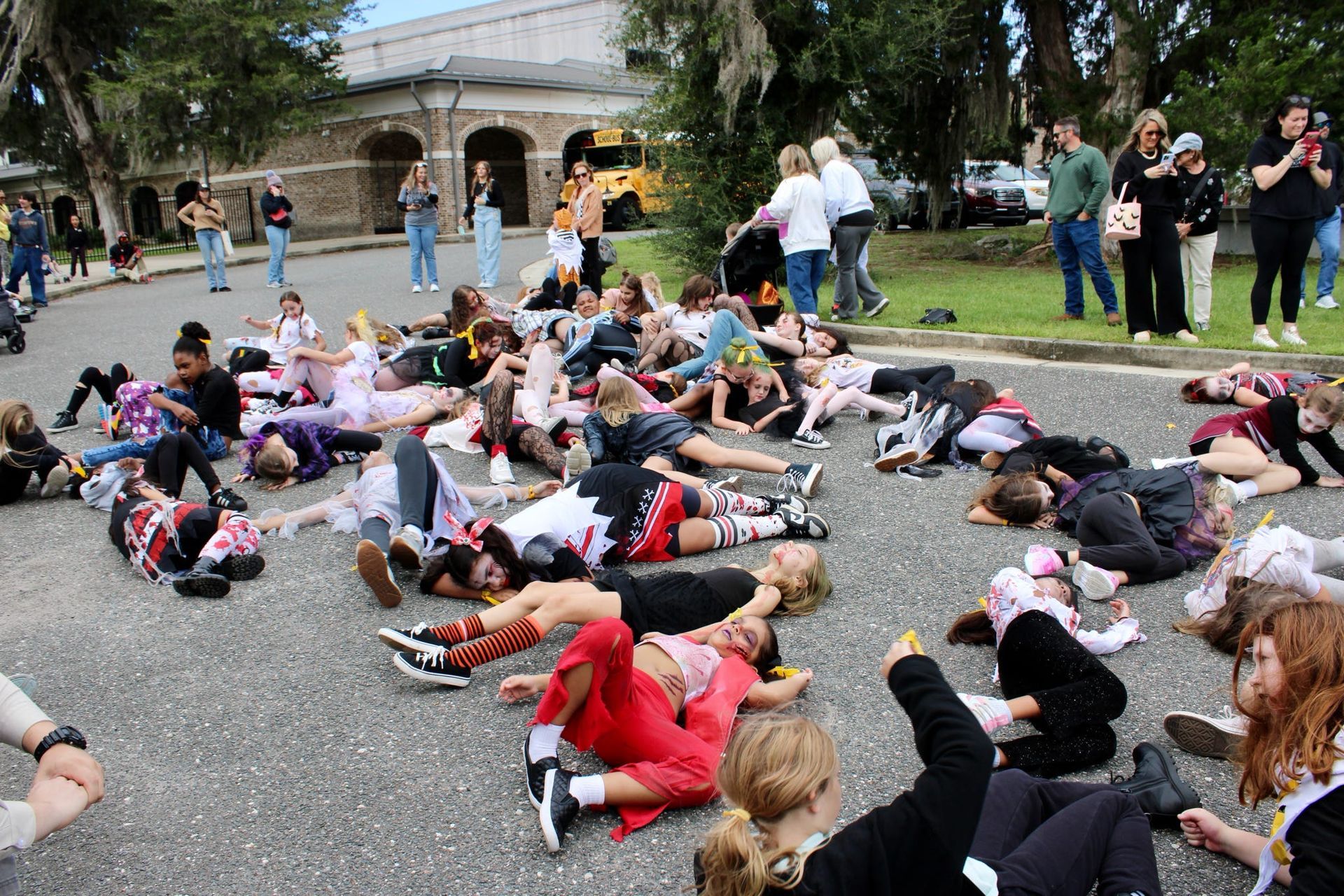 People lying on the ground in a park while others stand and watch near a building
