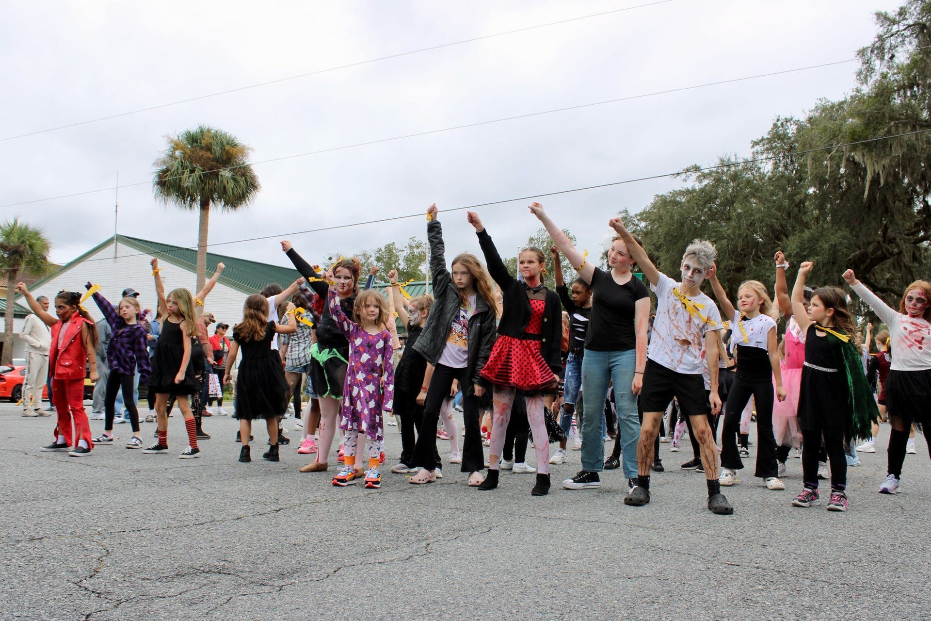 Group of people dancing outdoors on a street, many with arms raised in colorful costumes.