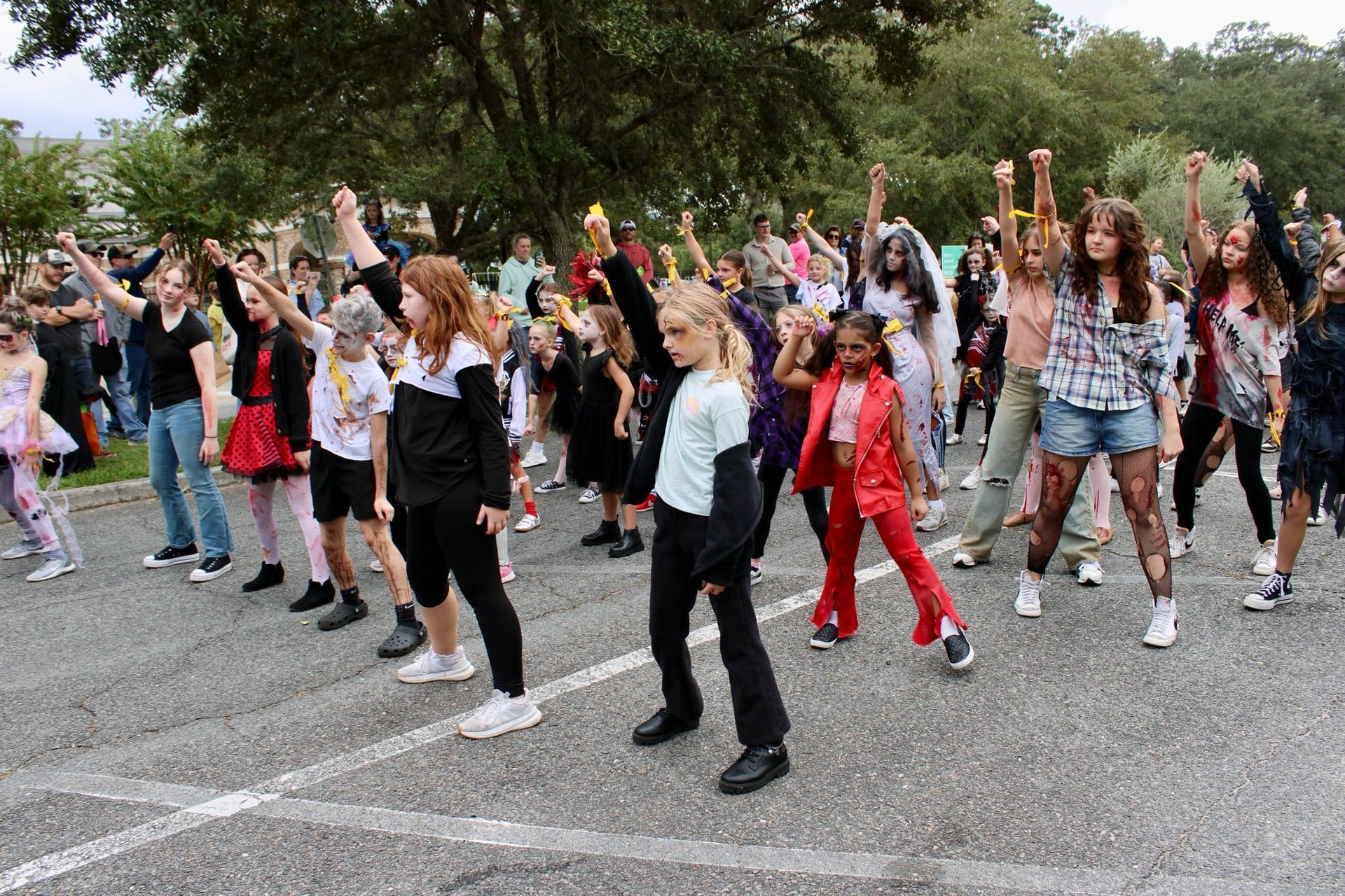 Group of people dancing outdoors in a parking lot, raising their arms in unison.