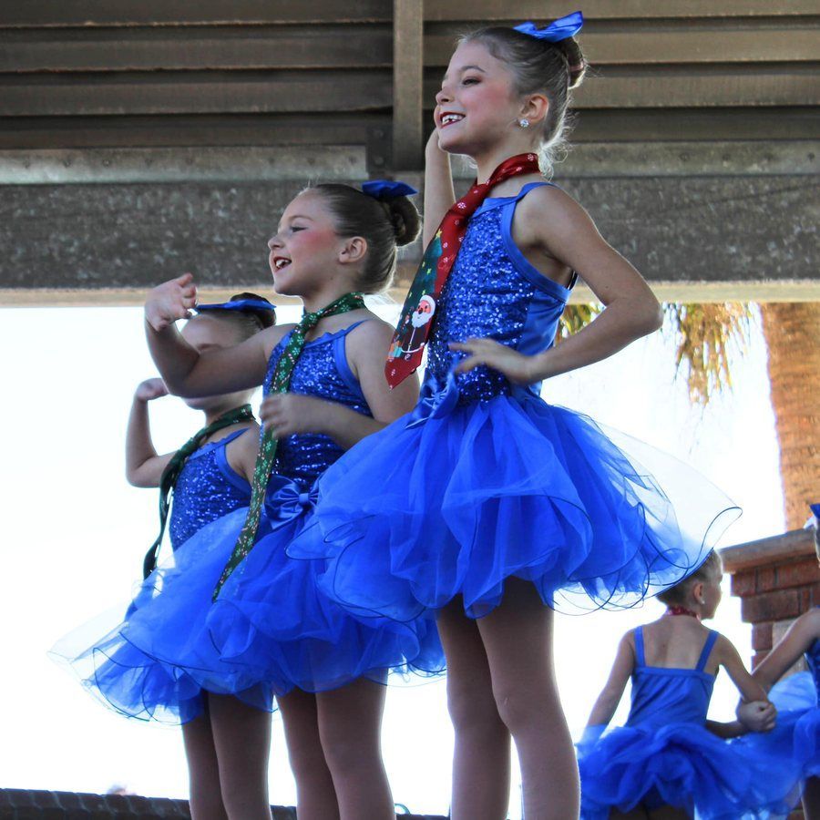 Children in blue dance costumes performing on a stage, smiling with hands on hips.