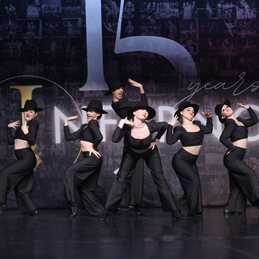 Six dancers in black costumes and hats pose on a stage with a 15 years backdrop.