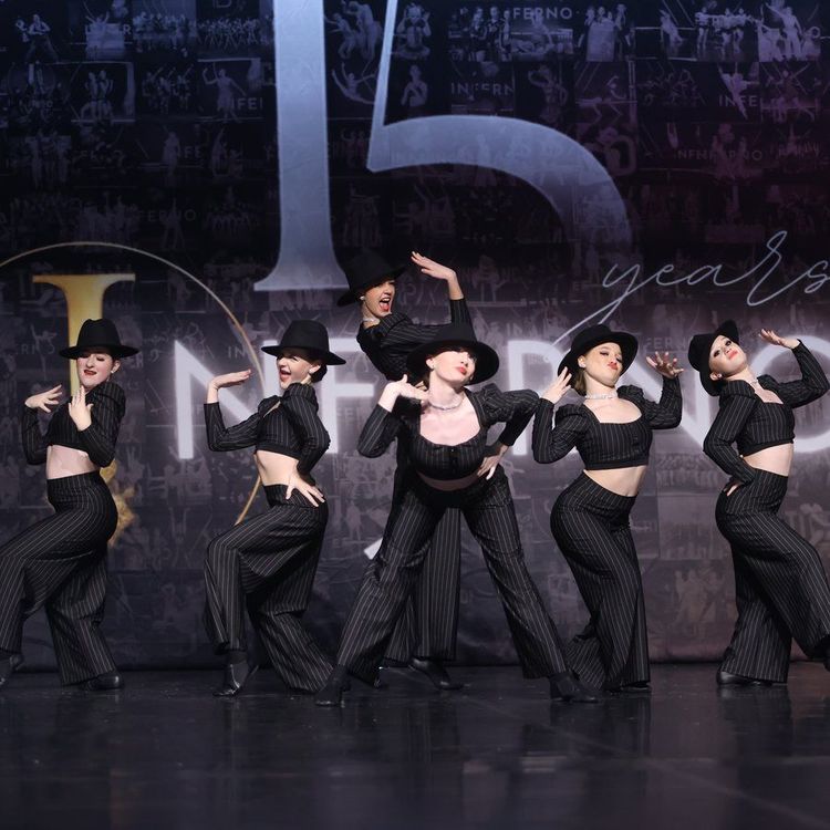 Six dancers in black costumes and hats pose on a stage with a 15 years backdrop.