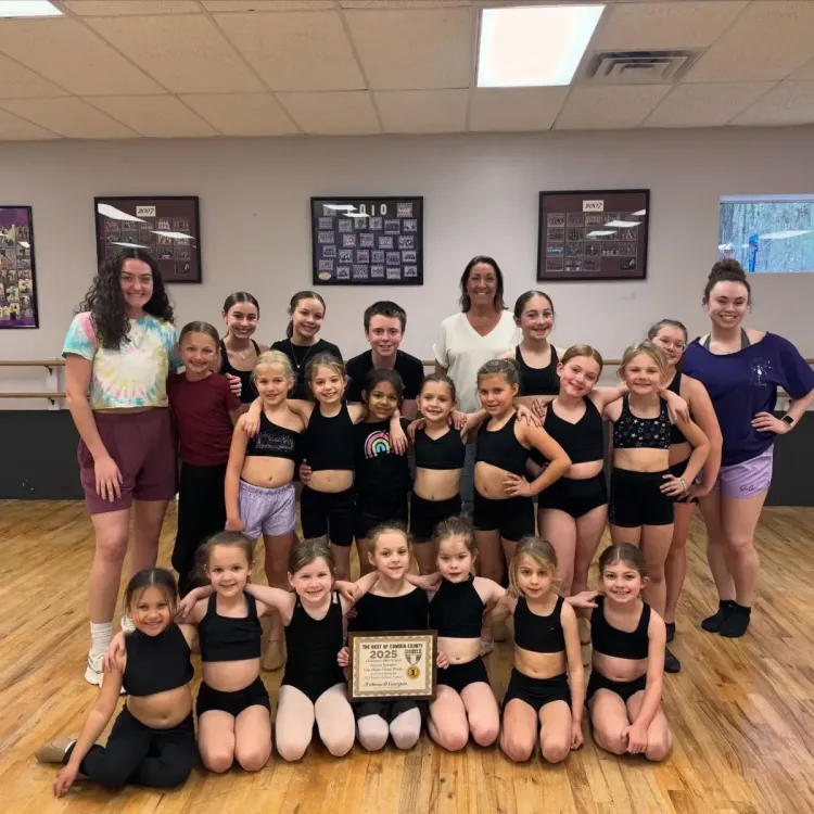 Smiling Lisa Allen's Dance Works students posing together in black dance attire against a purple backdrop