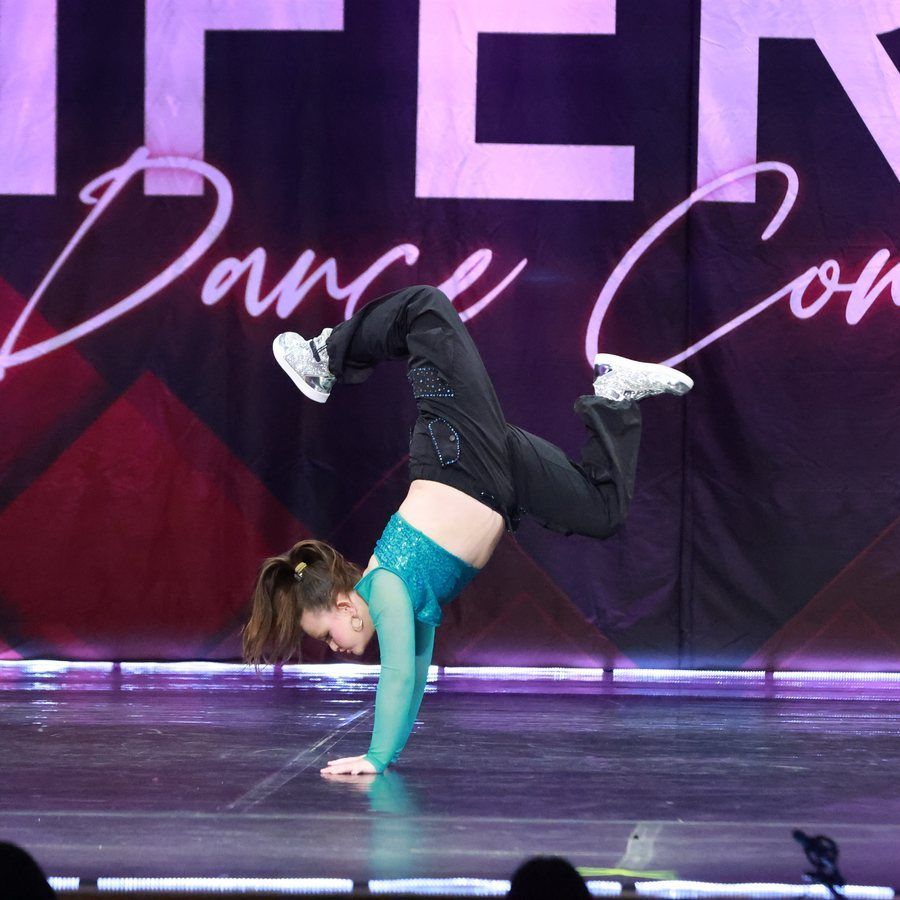 Contortionist balancing on one hand during a dance performance onstage, with purple backdrop.