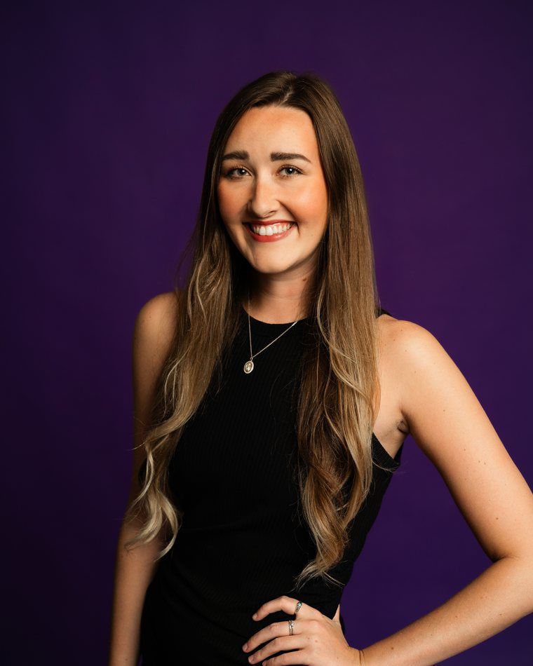 Smiling woman in a black sleeveless top posing against a purple background
