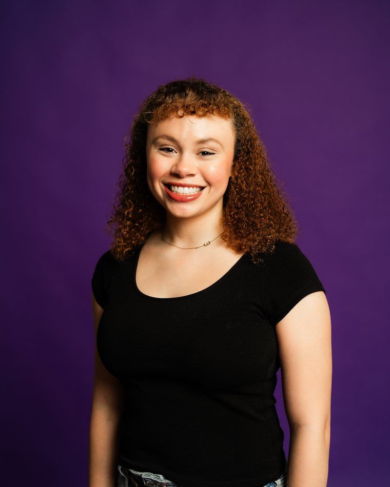 Smiling person in a black shirt against a purple background