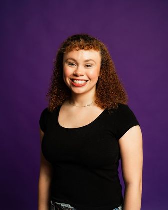 Smiling person in a black shirt against a purple background