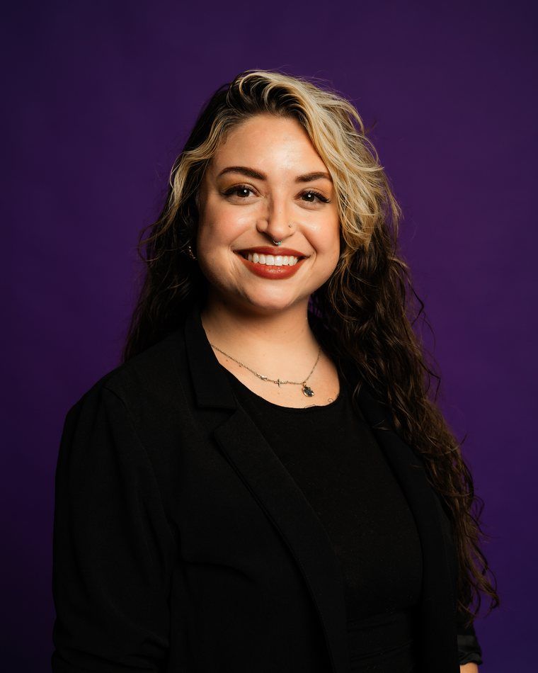 Smiling person in black clothing against a purple background
