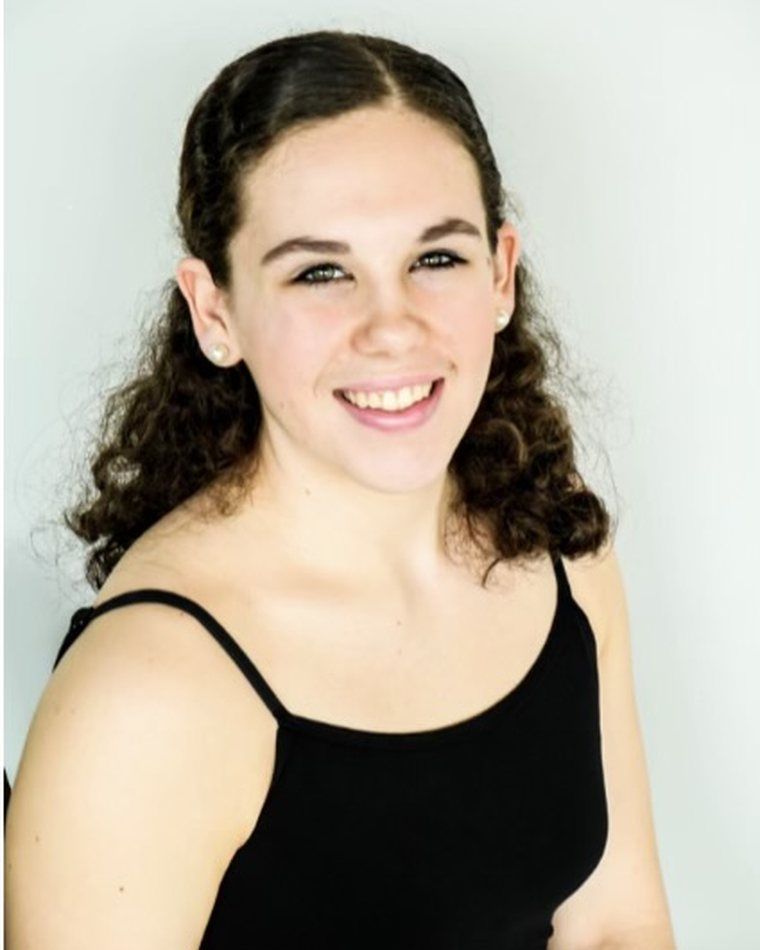 Smiling woman with curly dark hair in a black top against a light background