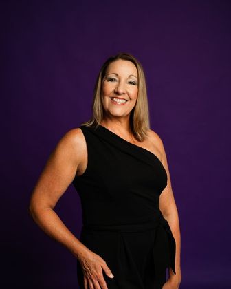 Smiling woman in a black one-shoulder dress against a purple studio backdrop
