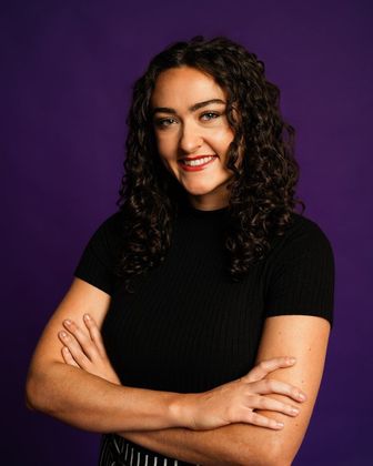 Smiling woman with curly hair and crossed arms against a purple background