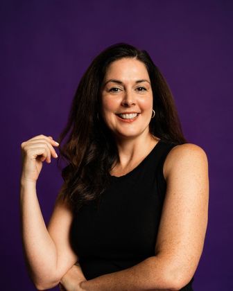 Smiling woman in a black sleeveless top posing against a purple studio backdrop