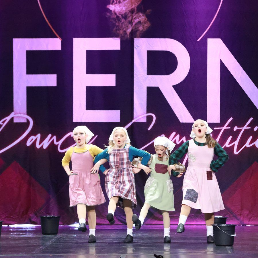 Four dancers in pastel costumes perform on a purple-lit stage with large FERN backdrop.