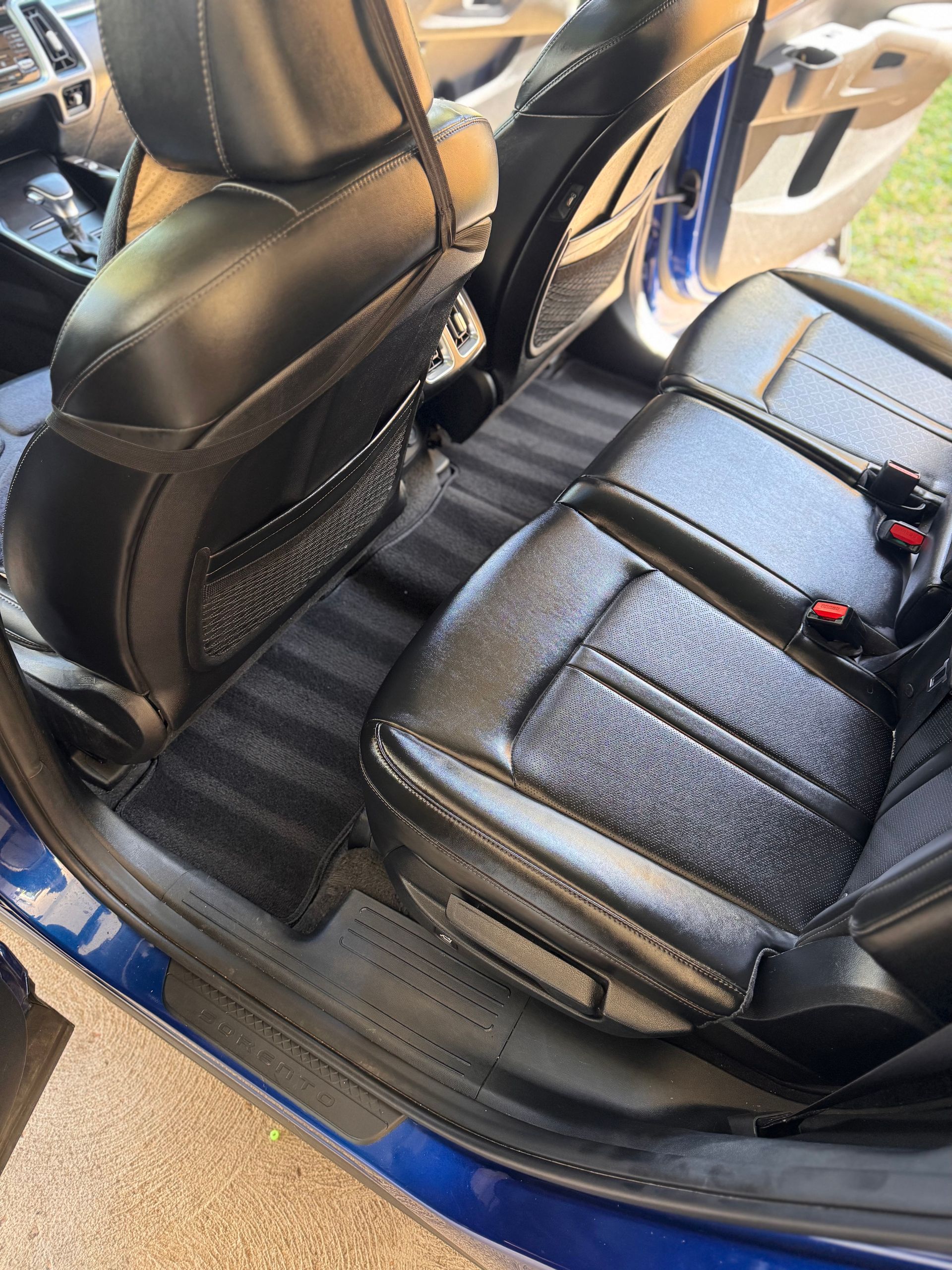 Black leather car seats and rear bench with blue trim, viewed from an open door