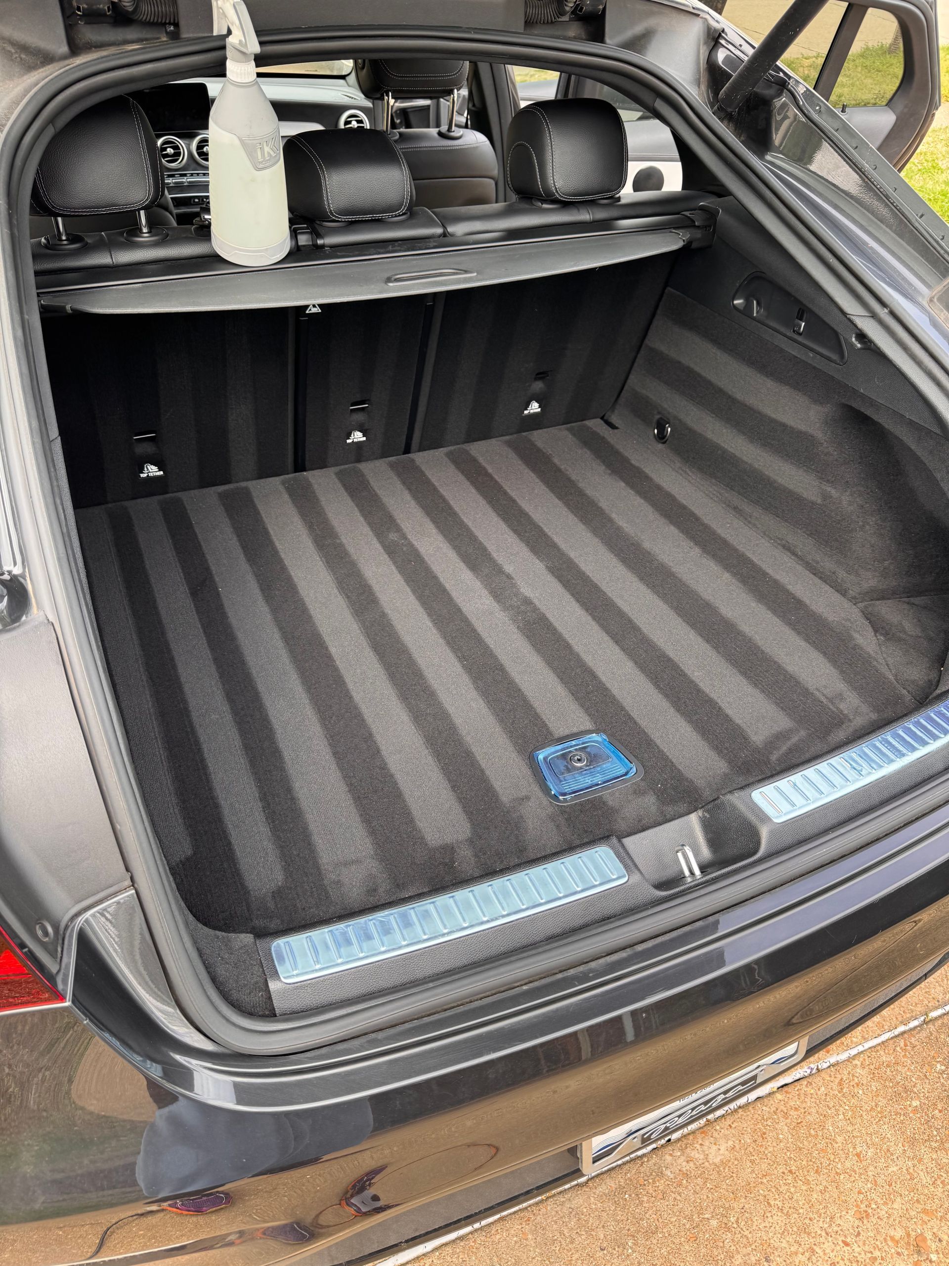 Open car trunk with striped cargo mat, bottle, and storage items on the rear shelf.
