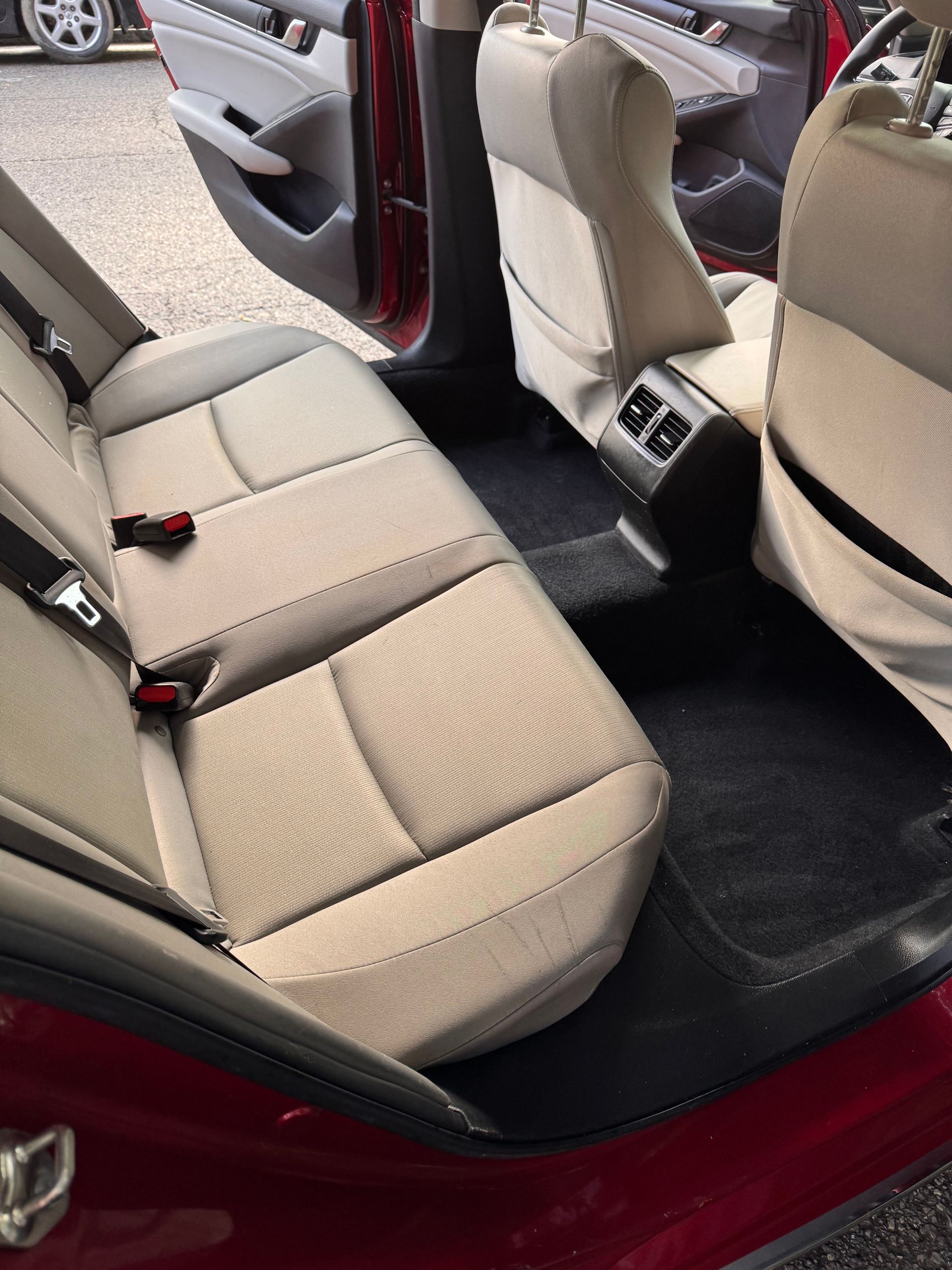 Rear car seats with beige upholstery and black floor mats, viewed through an open door.