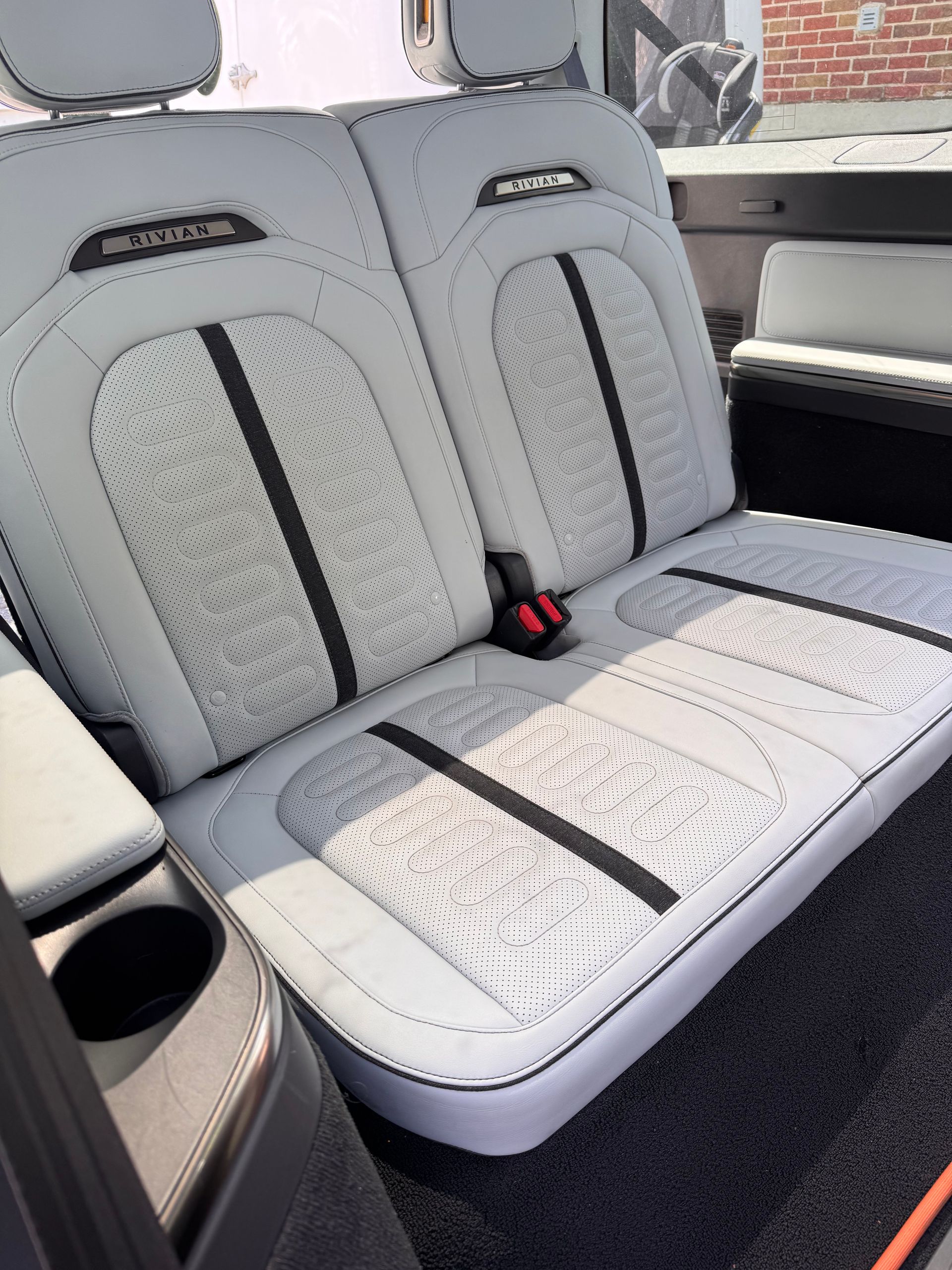 White leather car back seat with black accents and red seatbelt latch, viewed from the side.