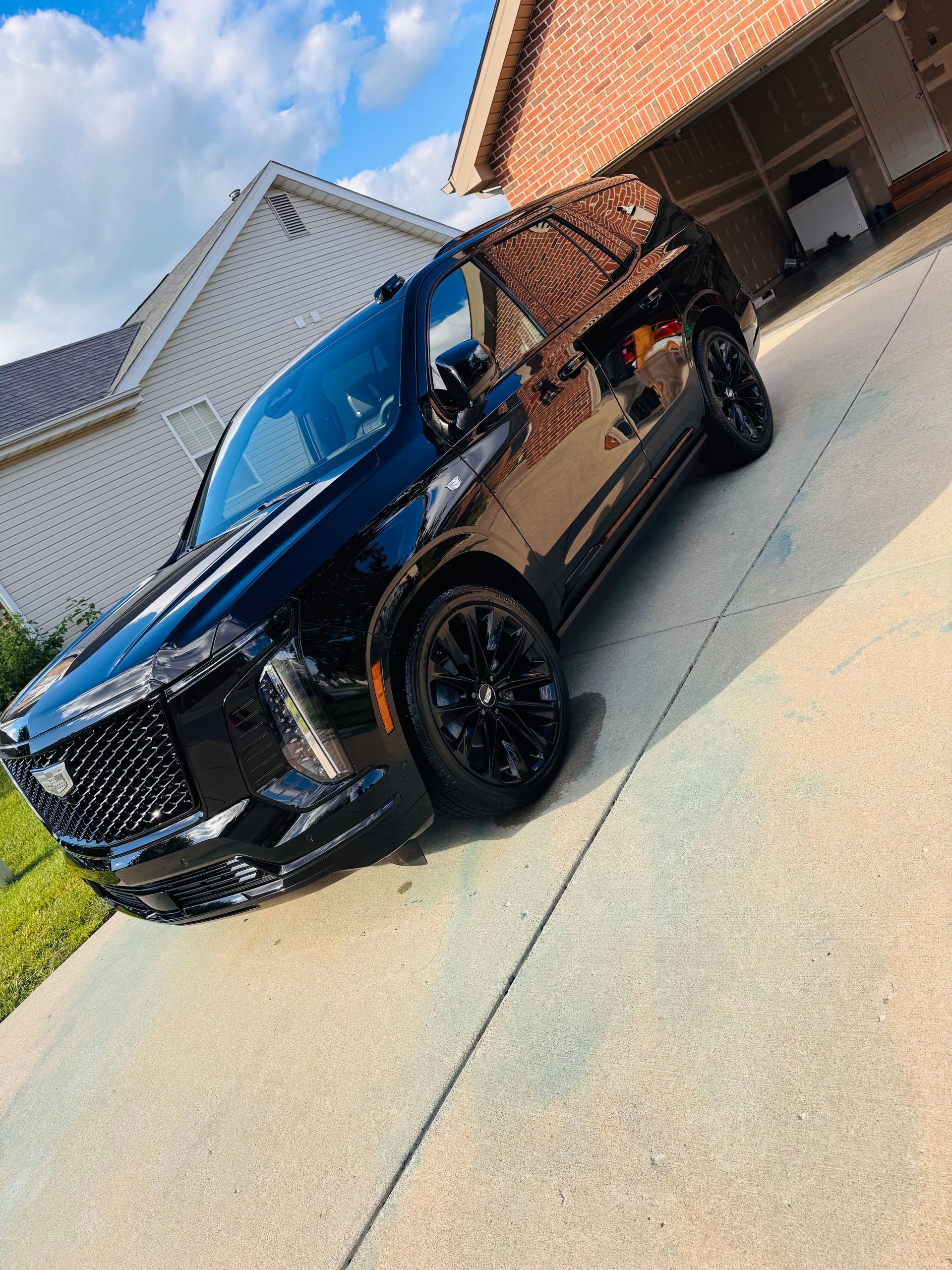 Black SUV parked in a driveway beside a house under a blue sky