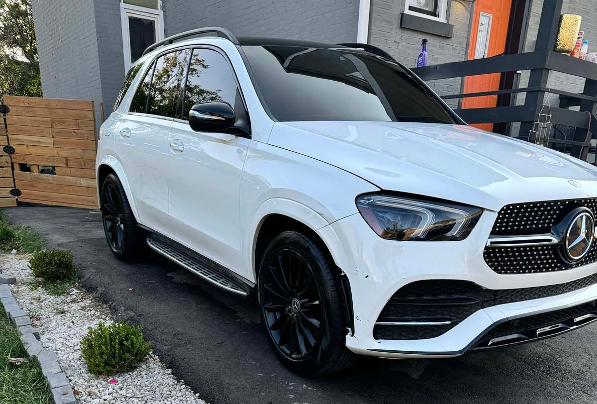 White Mercedes-Benz SUV parked on a street beside a house, with black wheels and tinted windows