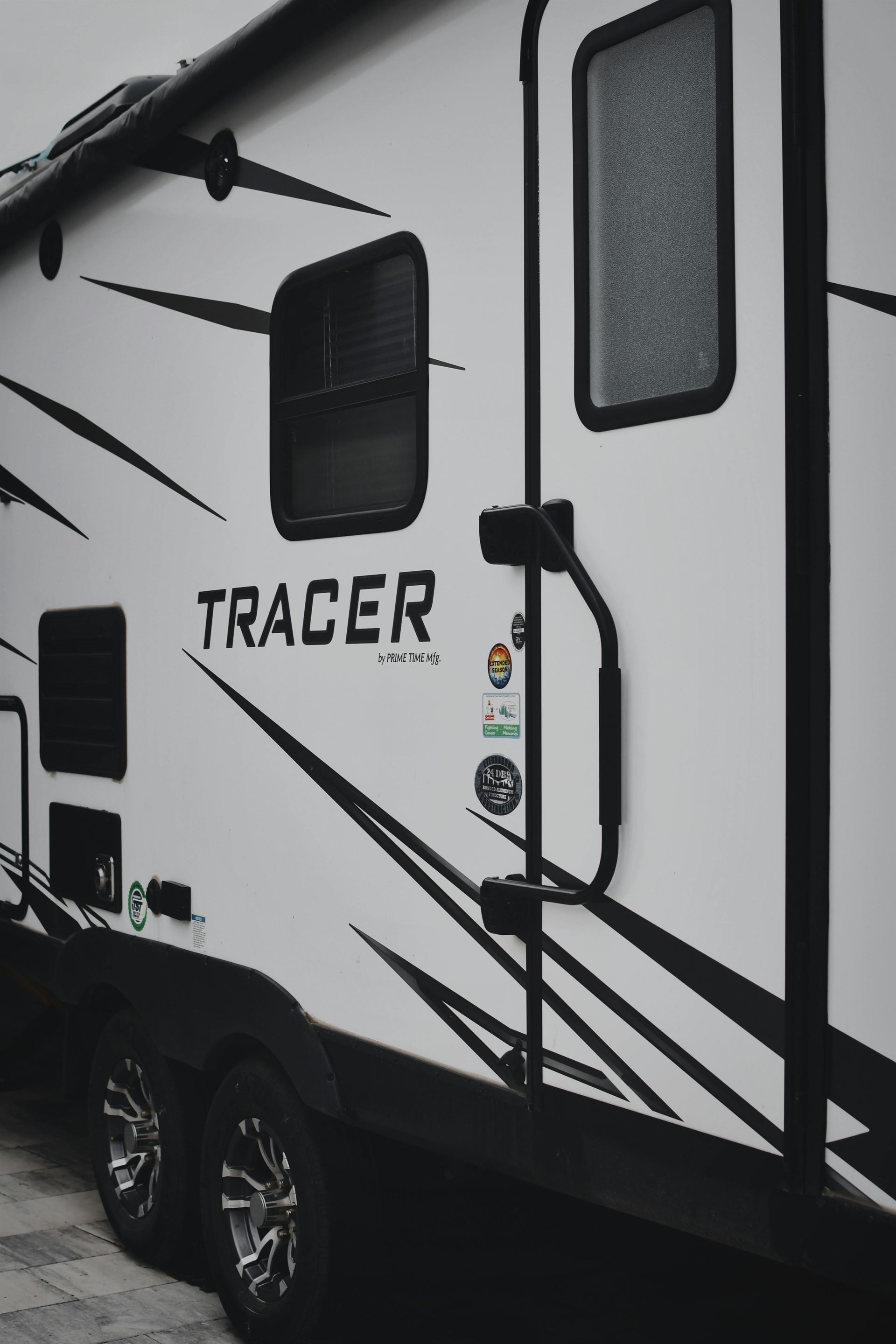 Side view of a white TRACER travel trailer with black accents and windows at a campsite